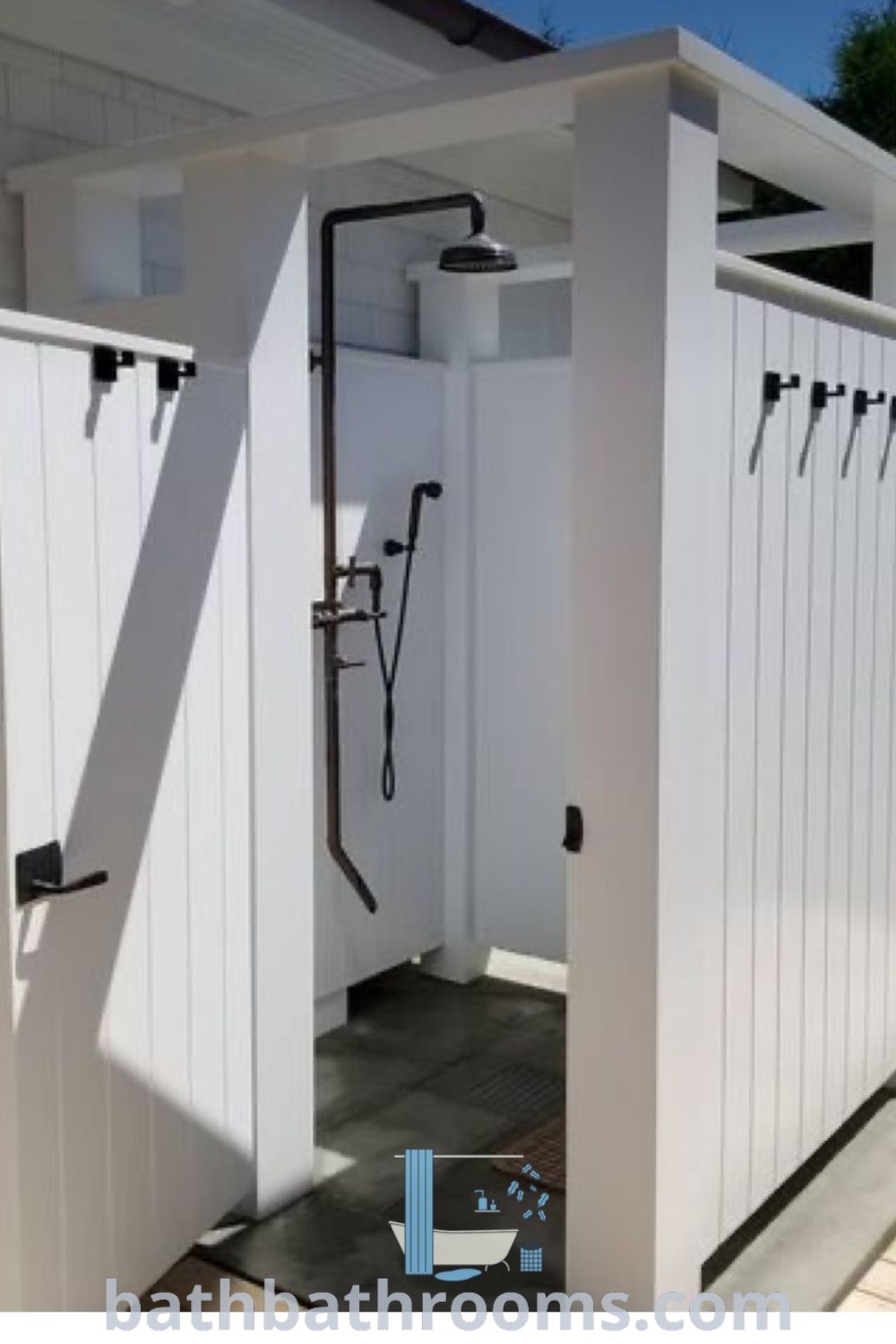 An outdoor shower inside a white shed with black handles and hooks, showcasing simple outdoor shower ideas for cozy aesthetics. Ideal for backyard tubs and outdoor bathroom inspirations. Explore design ideas at bathbathrooms.com.