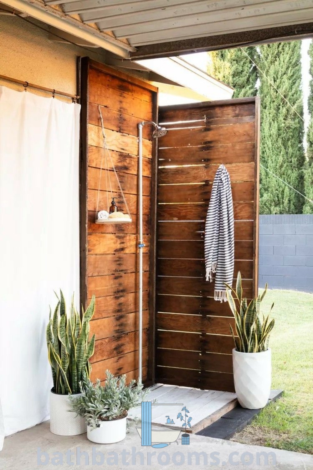 An inviting outdoor shower surrounded by two plants and a towel on the wall, highlighting cozy outdoor shower ideas for backyards. This outdoor shower inspiration offers a perfect blend of style and function for a refreshing experience. Discover more decor ideas at bathbathrooms.com.