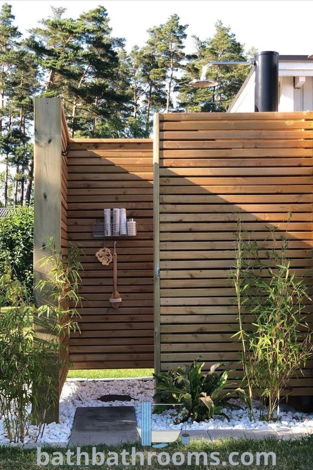 An outdoor shower in a yard with a stone floor, creating a cozy aesthetic in a garden bathroom outdoor style. Showcasing inspiring outdoor shower ideas, this setup offers a perfect style fusion for backyard pool shower concepts. Get design inspirations and ideas at bathbathrooms.com.