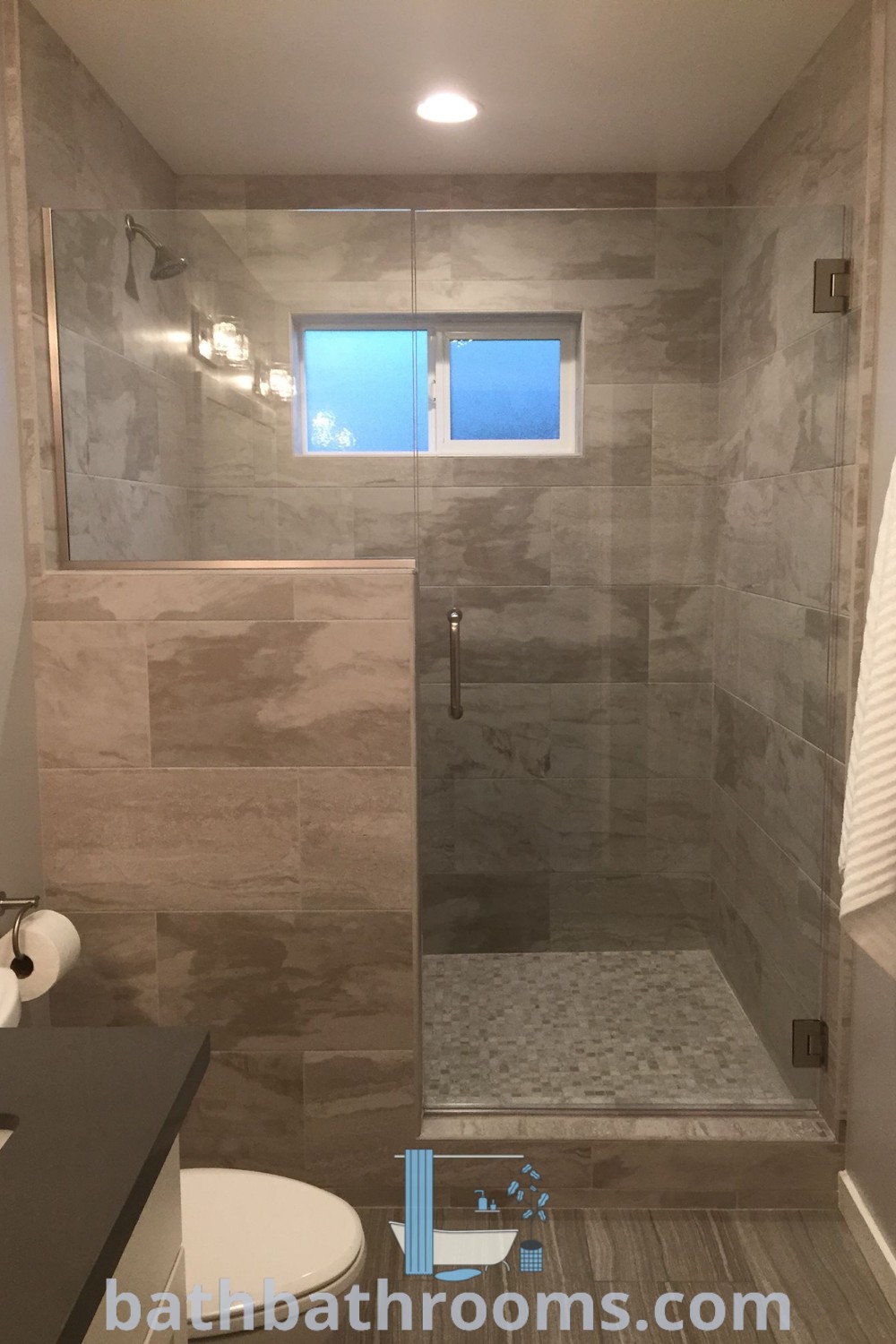 A stylish bathroom featuring a walk-in shower beside a toilet, showcasing modern enclosure ideas. This design maximizes space while offering a cozy aesthetic. Discover more unique bathroom design inspirations at bathbathrooms.com.