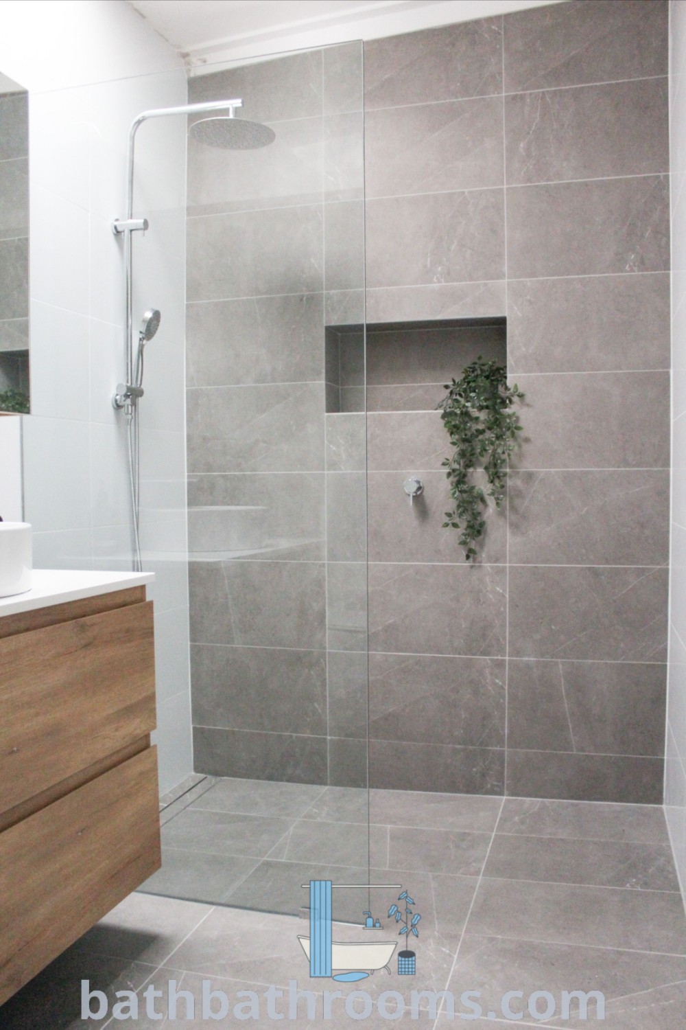 A modern zen bathroom showcasing a walk-in shower next to a white sink and a wooden cabinet, exemplifying light grey bathrooms and unique bathroom tile design ideas for maximizing space and style. Explore inspiring decor ideas at bathbathrooms.com.
