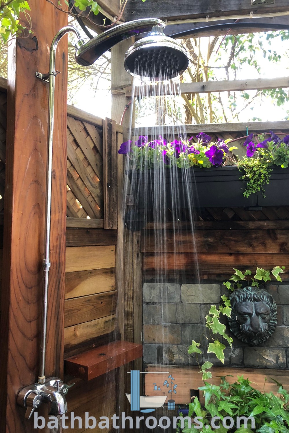 An outdoor shower with a decorative shower head releasing water, surrounded by blooming flowers on the wall, embodying a tropical house design. Perfect for camping grounds or outdoor baths, this charming setup delivers cozy decor inspirations for unique outdoor spaces. Explore more at bathbathrooms.com.