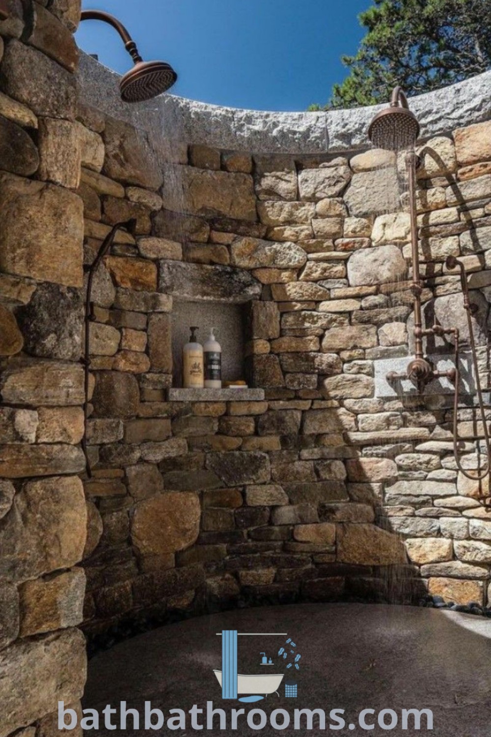 An outdoor shower with stone walls and exposed faucets, showcasing unique natural stone design elements. This inviting setup captures the essence of outdoor bathing with cozy inspirations and decor ideas from bathbathrooms.com.
