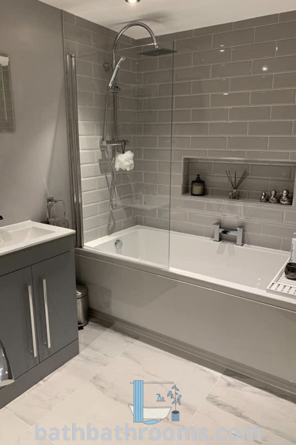 A modern grey scheme bathroom showcasing a sink, tub, and toilet adorned with grey tiles. This design features cozy inspirations and unique ideas, integrating modern family bathroom aesthetics. Find more decorating ideas for your home at bathbathrooms.com.