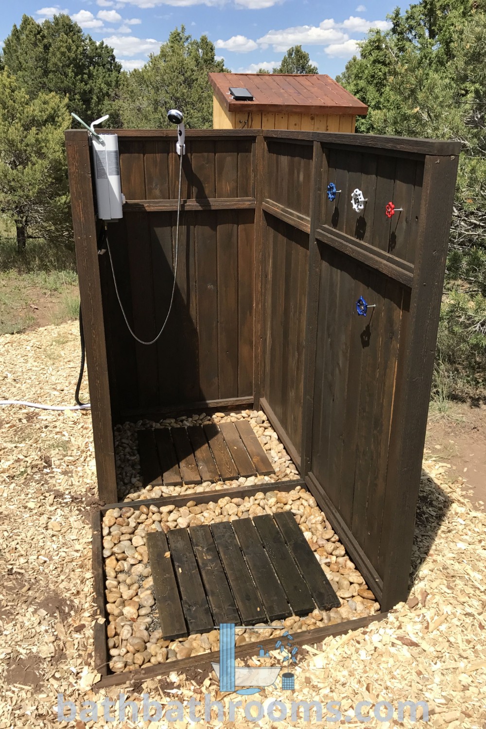 A wooden outhouse on a dirt field serving as an outdoor shower, exemplifying cozy decor ideas and unique design trends for a bathhouse. Explore outdoor shower ideas and inspirations for your home at bathbathrooms.com.