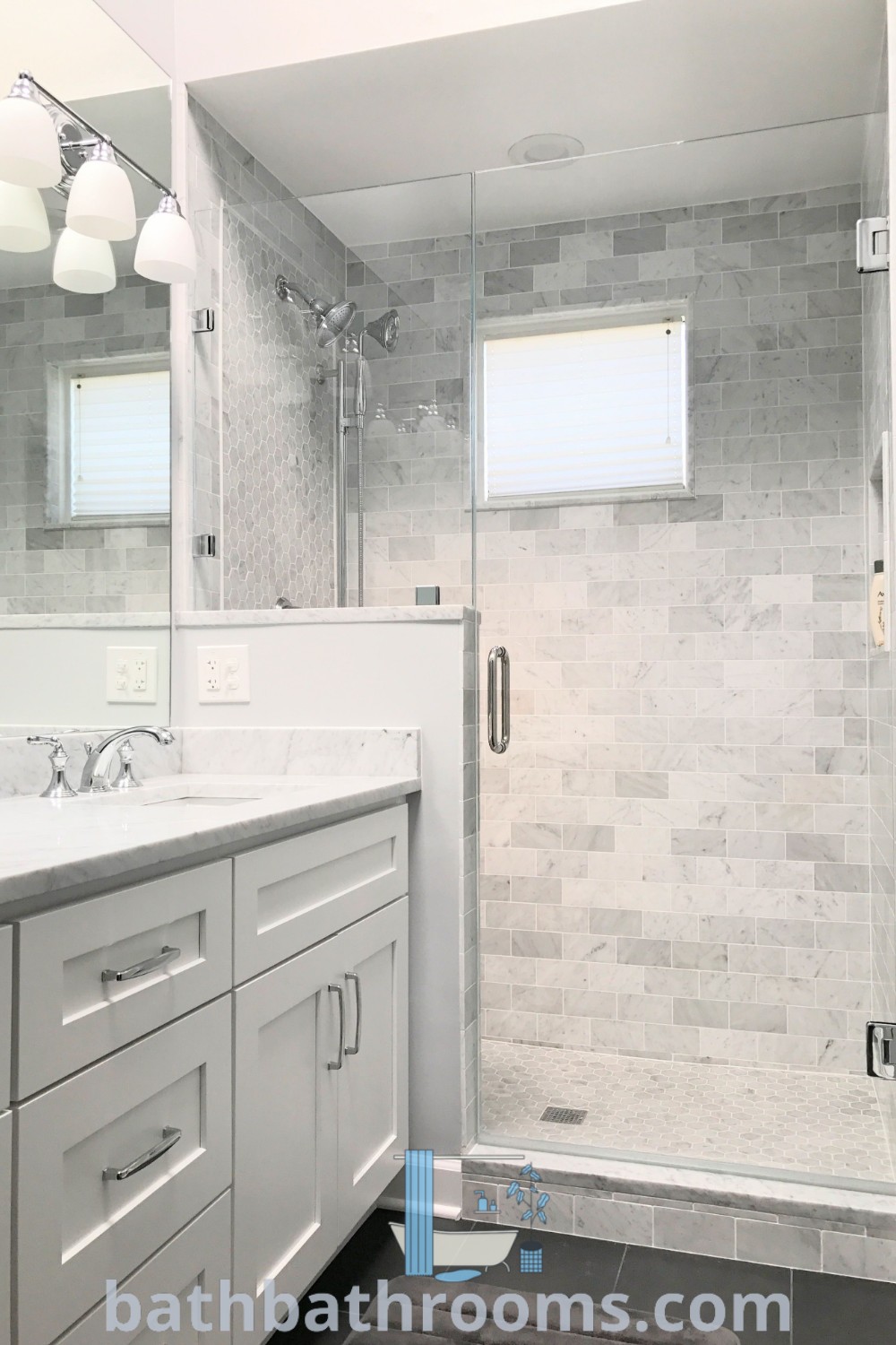 A stylish bathroom featuring a modern walk-in shower next to a white sink and countertop, illuminated under two lights. The frameless shower enclosures and glass shower enclosures showcase contemporary design ideas, making it an inspiring space for bathroom themes. Explore more on bathbathrooms.com.