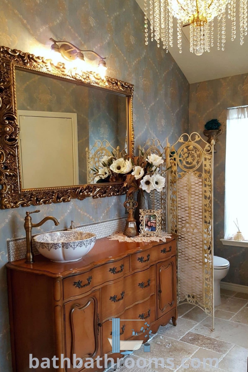 An ornate bathroom with a vanity, mirror, and chandelier reflects French Victorian style. The design showcases cozy decor ideas and vintage elements that inspire a perfect style fusion. Discover more unique inspirations at bathbathrooms.com.