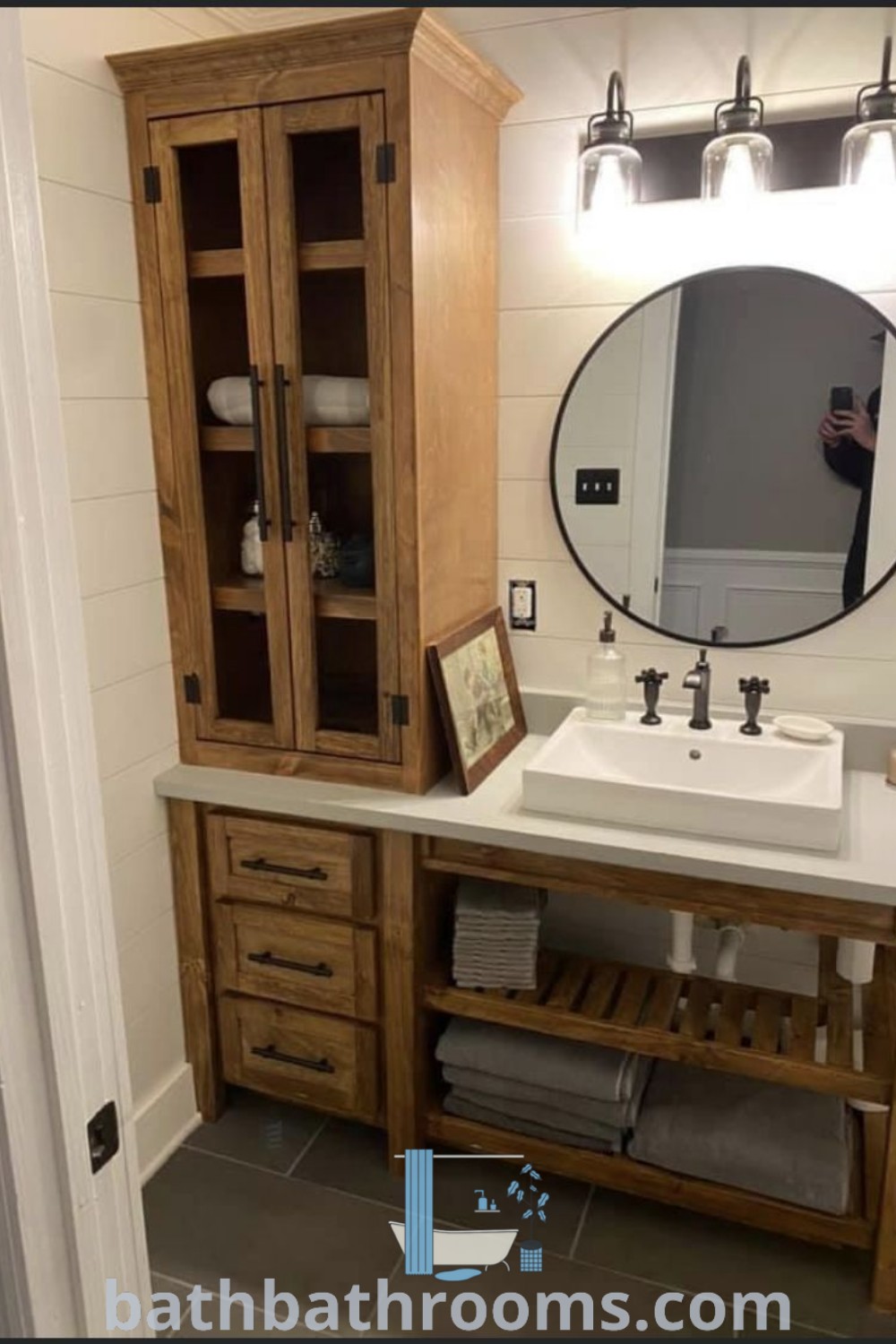 An elegant bathroom featuring a sink, mirror, and wooden cabinets, showcasing open bathroom cabinet ideas with rustic oak designs. The cozy aesthetic emphasizes both style and functionality. Explore unique inspirations and decor ideas for your home at bathbathrooms.com.