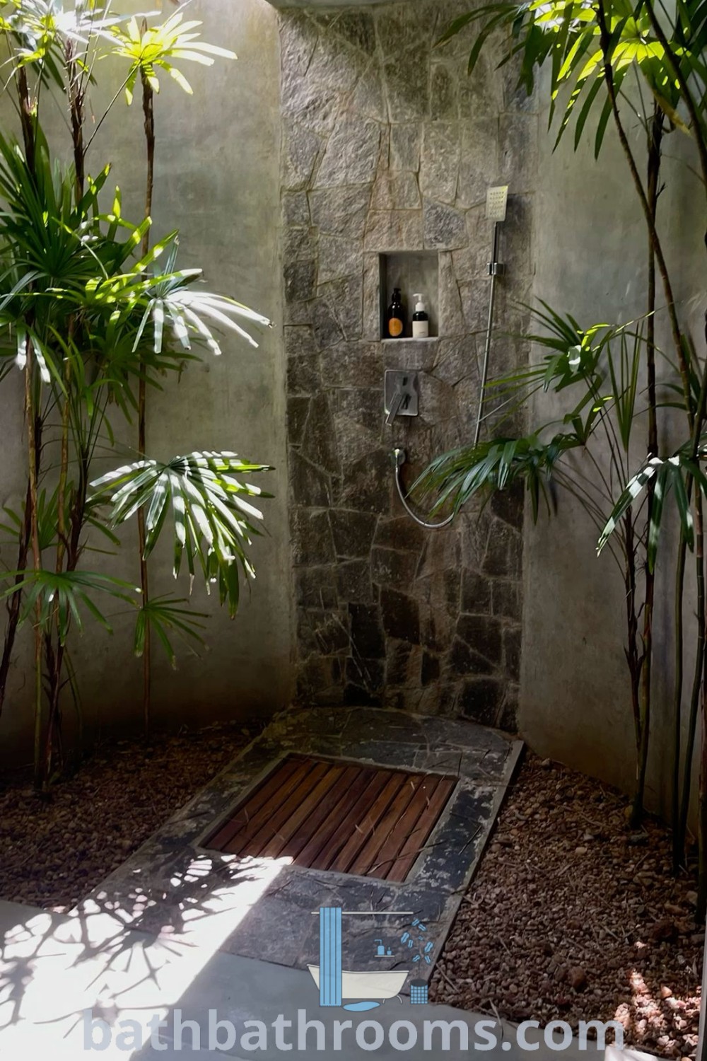 An elegant outdoor shower surrounded by plants and rocks that embodies a Balinese bathroom aesthetic. This design showcases outdoor shower inspiration with a cozy and tranquil ambiance. Discover more decor ideas at bathbathrooms.com.