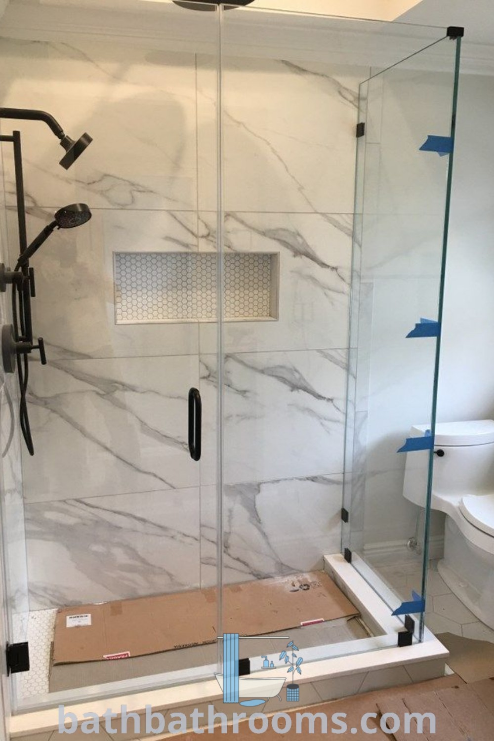 A stylish bathroom with a modern walk-in shower, frameless shower doors, a toilet, and a sink under construction. The design offers unique ideas for farmhouse master baths and custom shower solutions, showcasing a cozy aesthetic. Discover more at bathbathrooms.com.