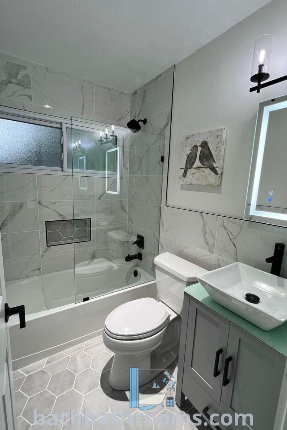 A modern bathroom featuring a white toilet, a walk-in shower, and a sink under a mirror, decorated with big tiles. This remodel exemplifies cozy ideas and modern restroom inspirations perfect for small full bathrooms. Discover more design tips at bathbathrooms.com.