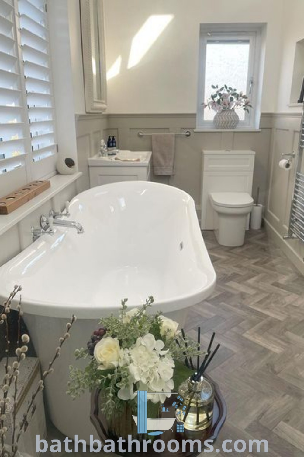 A large white bath tub with a toilet in a luxurious modern country bathroom, set on hardwood flooring, reflecting elegant cottage bathroom design ideas. This cozy aesthetic showcases panelled bathroom inspirations for a perfect style fusion. Discover more decor ideas at bathbathrooms.com.
