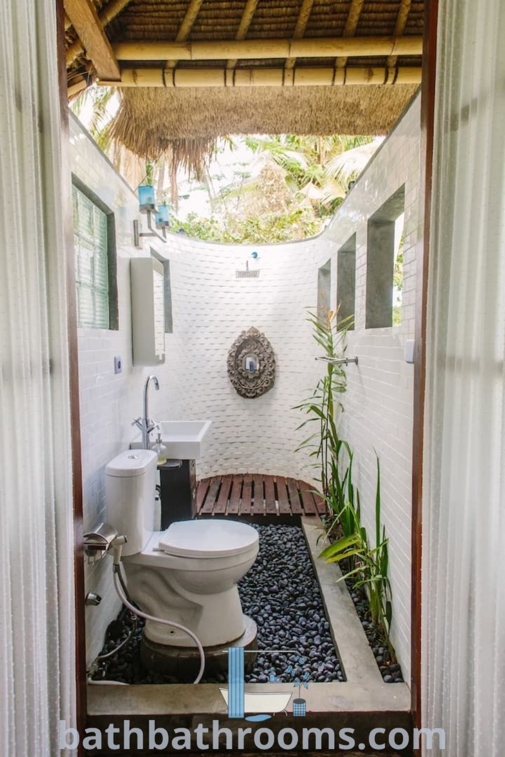 An outdoor pool bathroom with a white toilet and sink next to a bamboo roof, showcasing design ideas for a serene outdoor bathroom experience. This unique setup combines outdoor toilet and shower elements for a cozy aesthetic. Discover more at bathbathrooms.com.