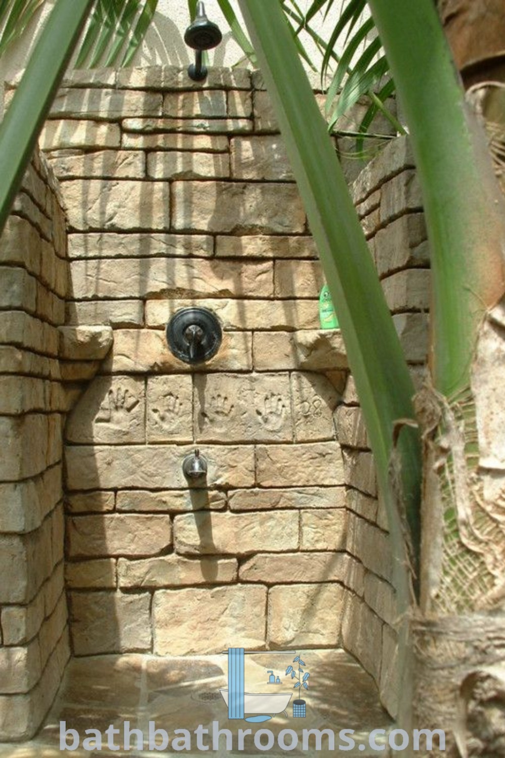 An outdoor shower shaped like a brick wall featuring handprint tiles, providing unique outdoor shower ideas. This stylish rock shower is a perfect addition to outdoor bathroom design, enhancing the space
