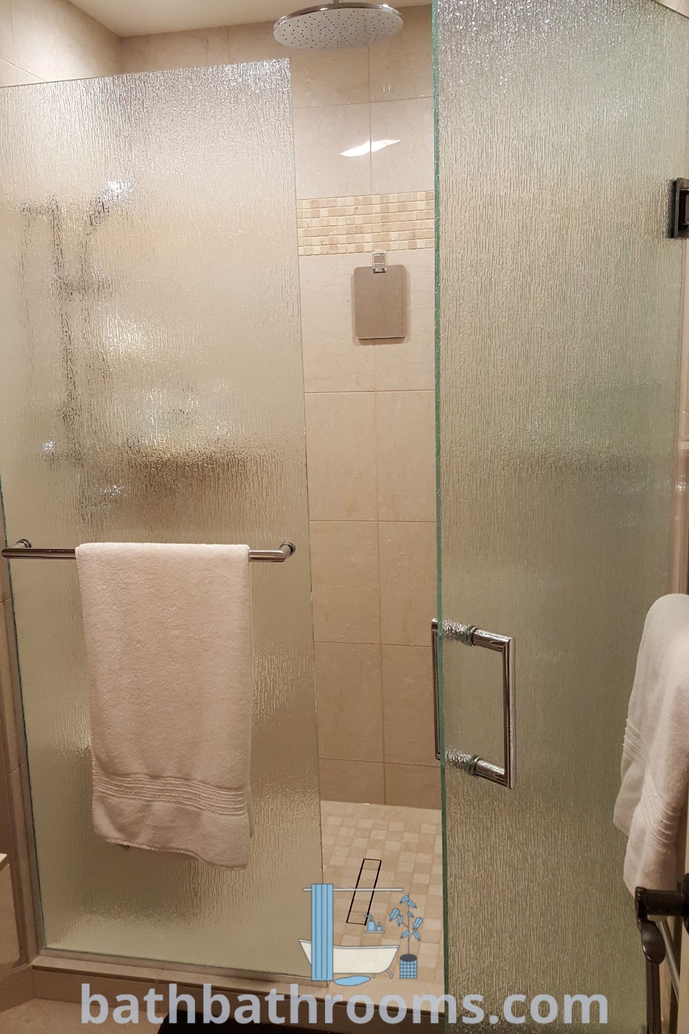 An elegant rain glass shower door in a bathroom beside a towel rack, showcasing frosted shower doors that enhance privacy and modern design. This setup offers inspiring ideas for small shower remodels and a cozy aesthetic. Discover more unique decor ideas at bathbathrooms.com.