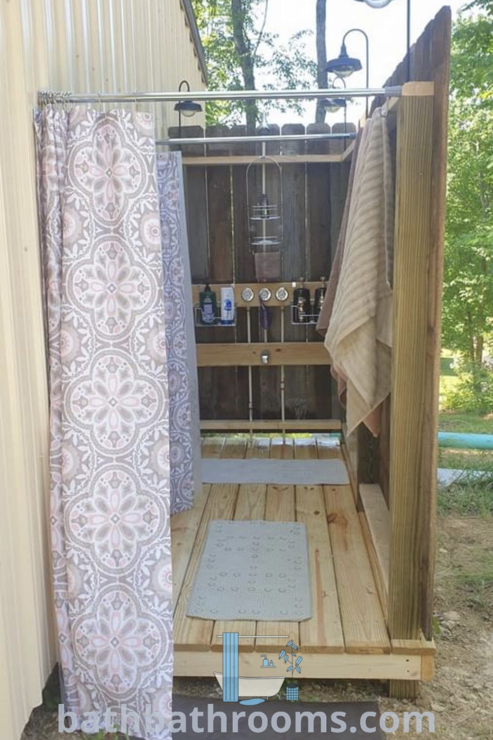 An outdoor shower built into the side of a building with curtains hanging on its sides, featuring cozy decor ideas for a relaxing outdoor bathroom design. Explore this inspiring setup and discover unique ideas at bathbathrooms.com.