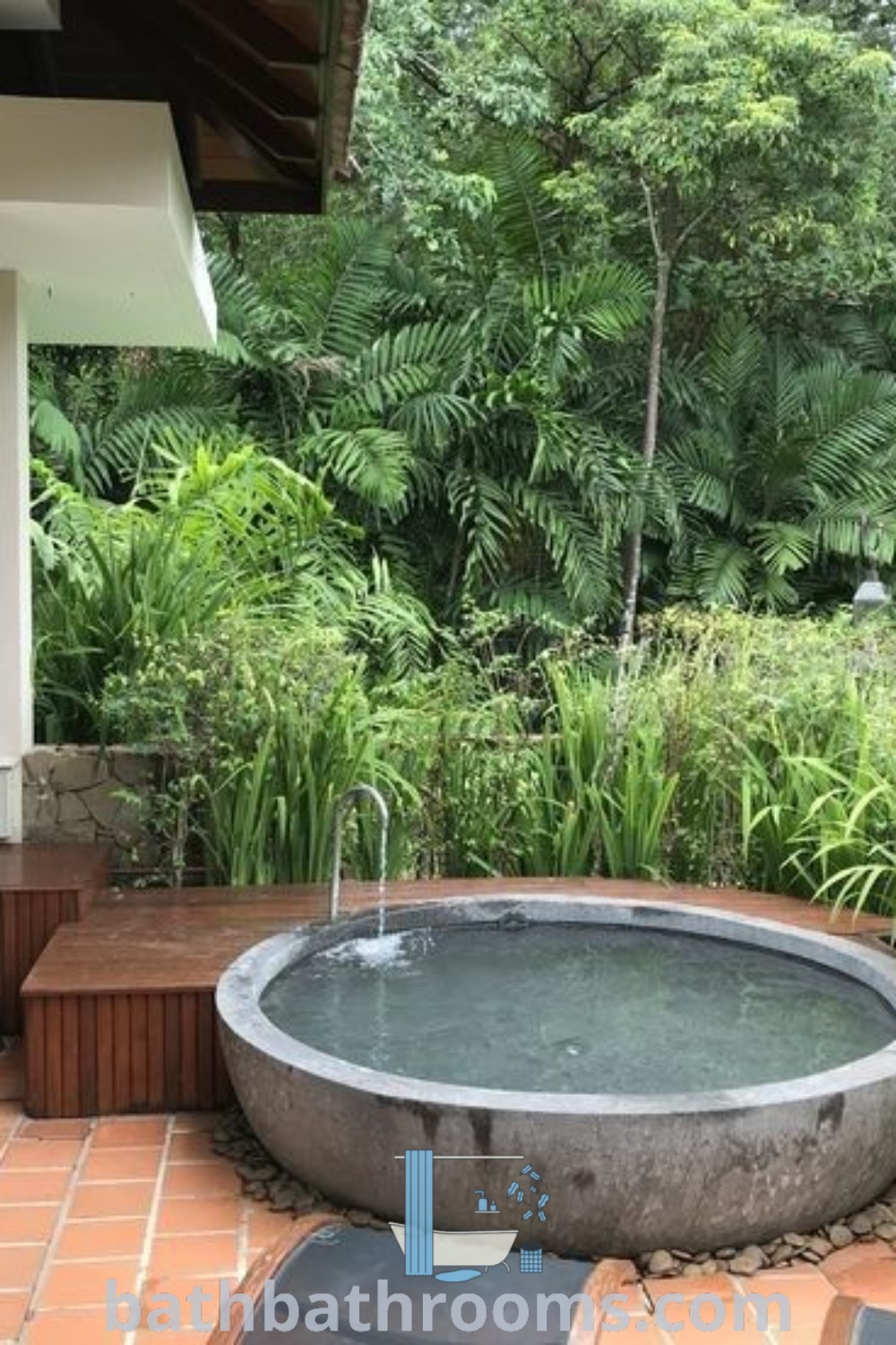 A round spa outdoor hot tub sitting on a brick patio beside a lush green forest, representing the perfect outdoor bath tub ideas for a cozy retreat. Explore unique design inspirations and cozy outdoor decor ideas at bathbathrooms.com.