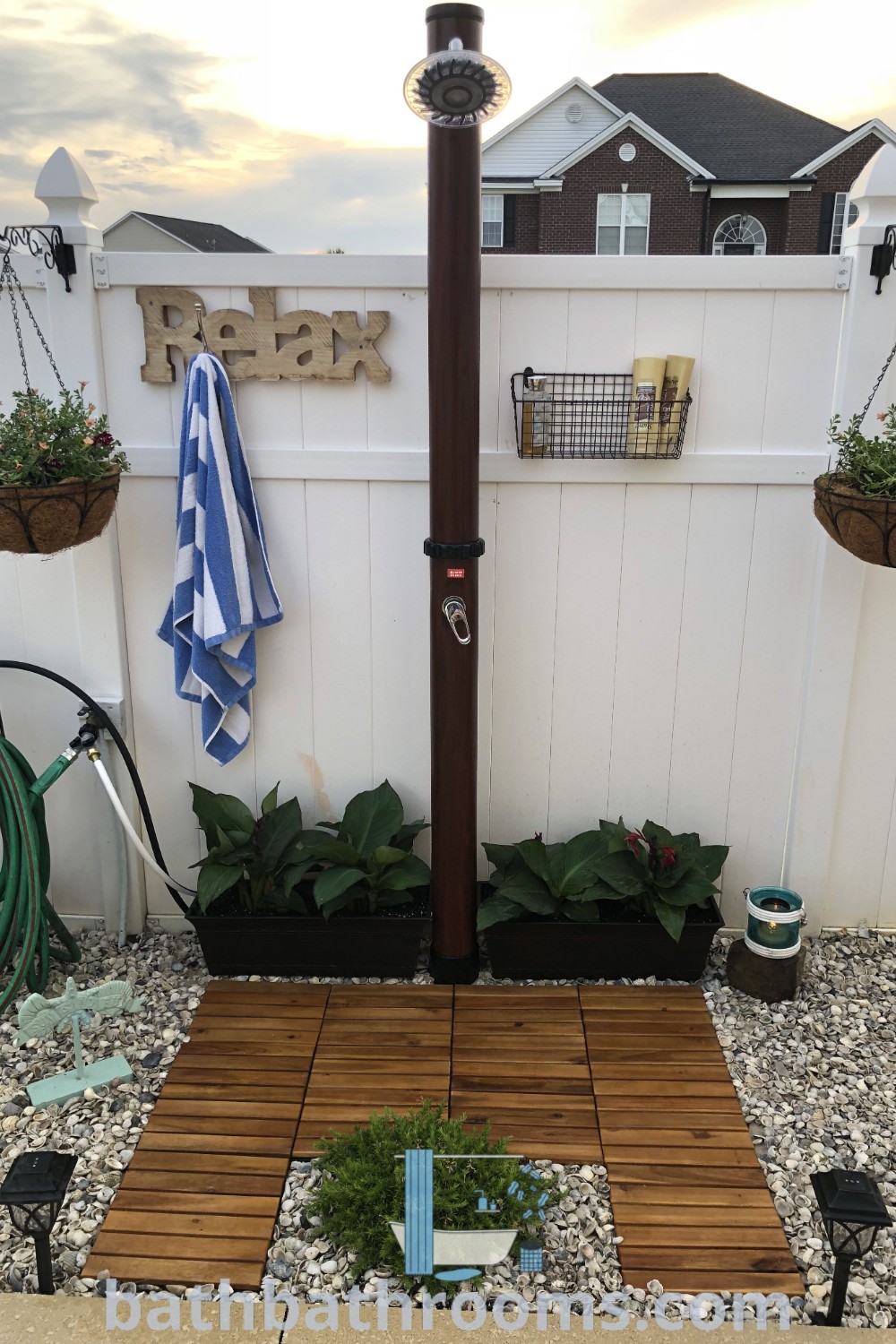 An inviting outdoor shower in a garden setting, equipped with plants, hoses, and a bench, featuring cozy and inspiring decor ideas for an outdoor space. Explore more unique outdoor shower designs at bathbathrooms.com.