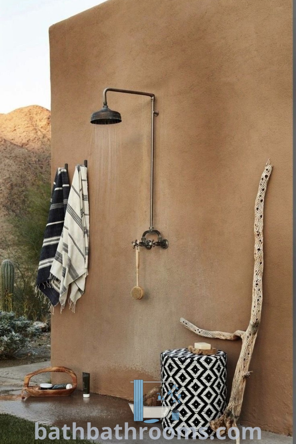 An outdoor shower with black and white towels hanging on the wall next to a cactus, inspired by Greek cottage decor and cozy outdoor shower ideas. Explore unique design ideas and inspiration for transforming your home at bathbathrooms.com.