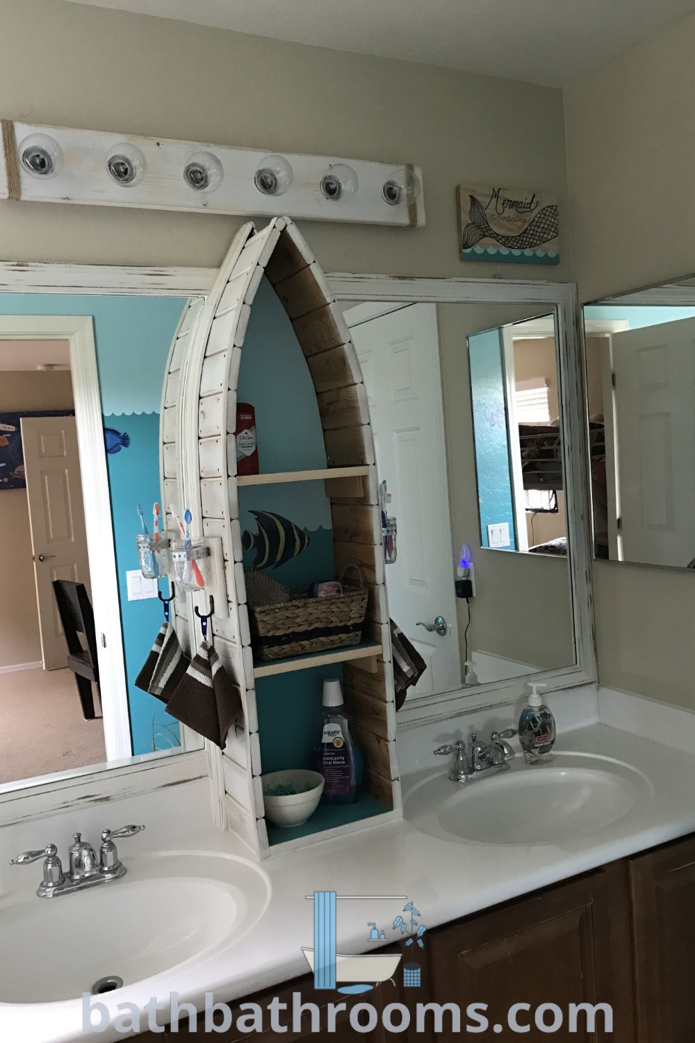 A cozy nautical themed bathroom featuring two sinks, a large mirror, and decor inspired by Greece, boats, and fishing. Ideal for creating a lake or water bathroom theme, it offers design ideas that maximize both style and space. Discover more decor inspirations at bathbathrooms.com.