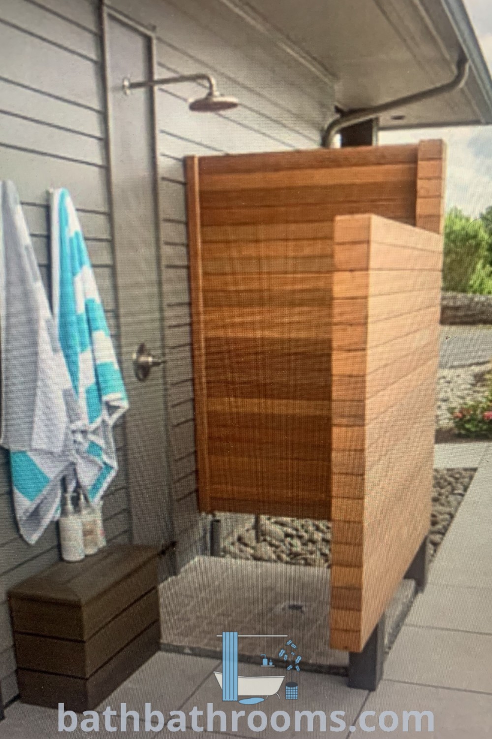 An outdoor shower with towels hanging on the wall and an open shower door, creating a cozy beach house vibe. The contemporary design offers functional outdoor shower ideas that inspire creation of a serene and inviting atmosphere. Discover more decor ideas at bathbathrooms.com.