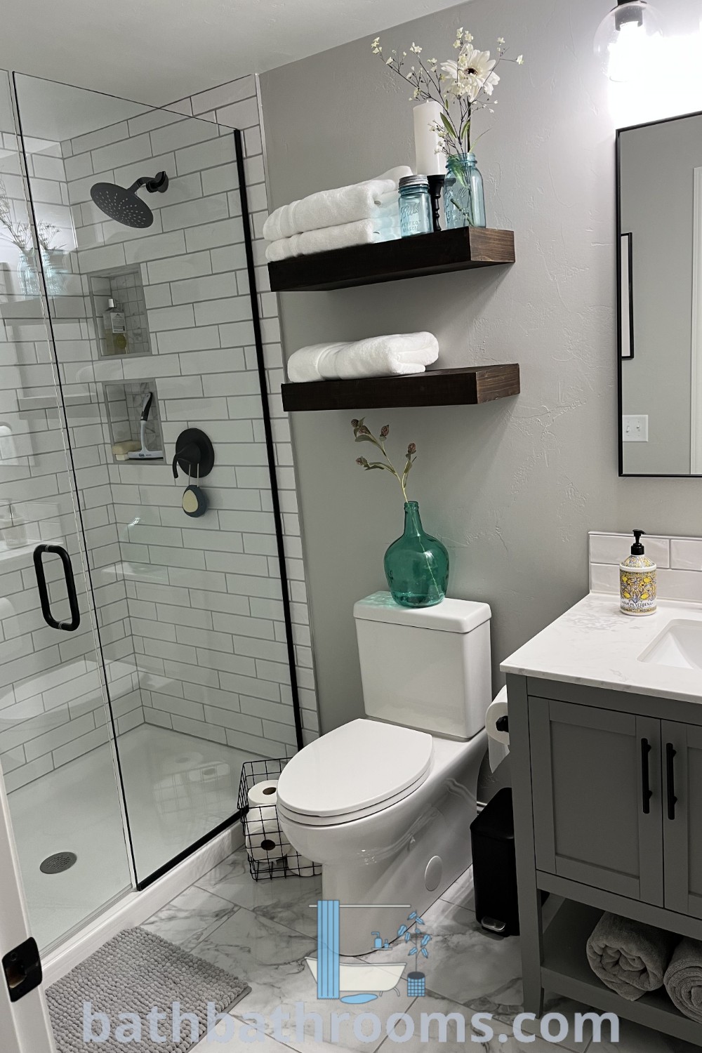 A stylish small bathroom showcasing a white toilet under a bathroom mirror, adjacent to a walk-in shower and sink. This cozy design maximizes style and space, ideal for small bathroom renovations. Explore more cozy decor ideas and inspirations at bathbathrooms.com.