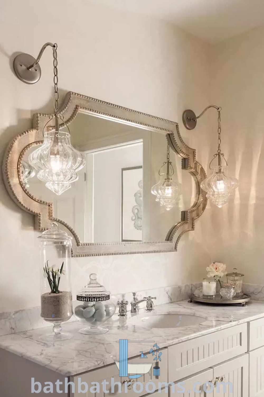 An elegant bathroom with marble countertops and white cabinets, two wall lights, and a large mirror over the sink, showcasing French country bathroom design. Discover more cozy decor ideas for your home at bathbathrooms.com.