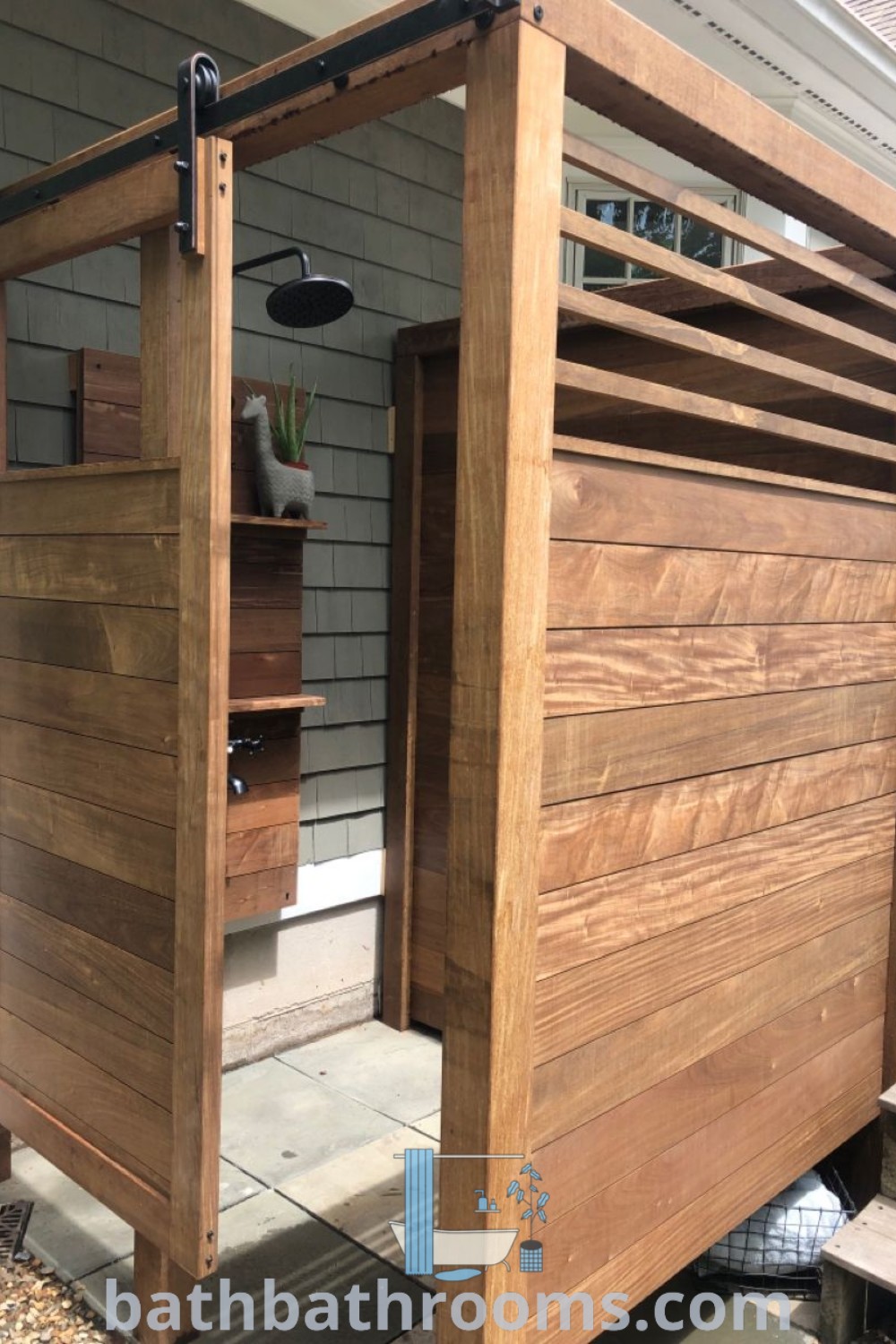 A charming wooden outdoor shower structure beside a house, ideal for outdoor bathroom design and changing rooms. This cozy aesthetic is perfect for cottage showers and inspiring outdoor shower ideas. Discover more design inspirations at bathbathrooms.com.