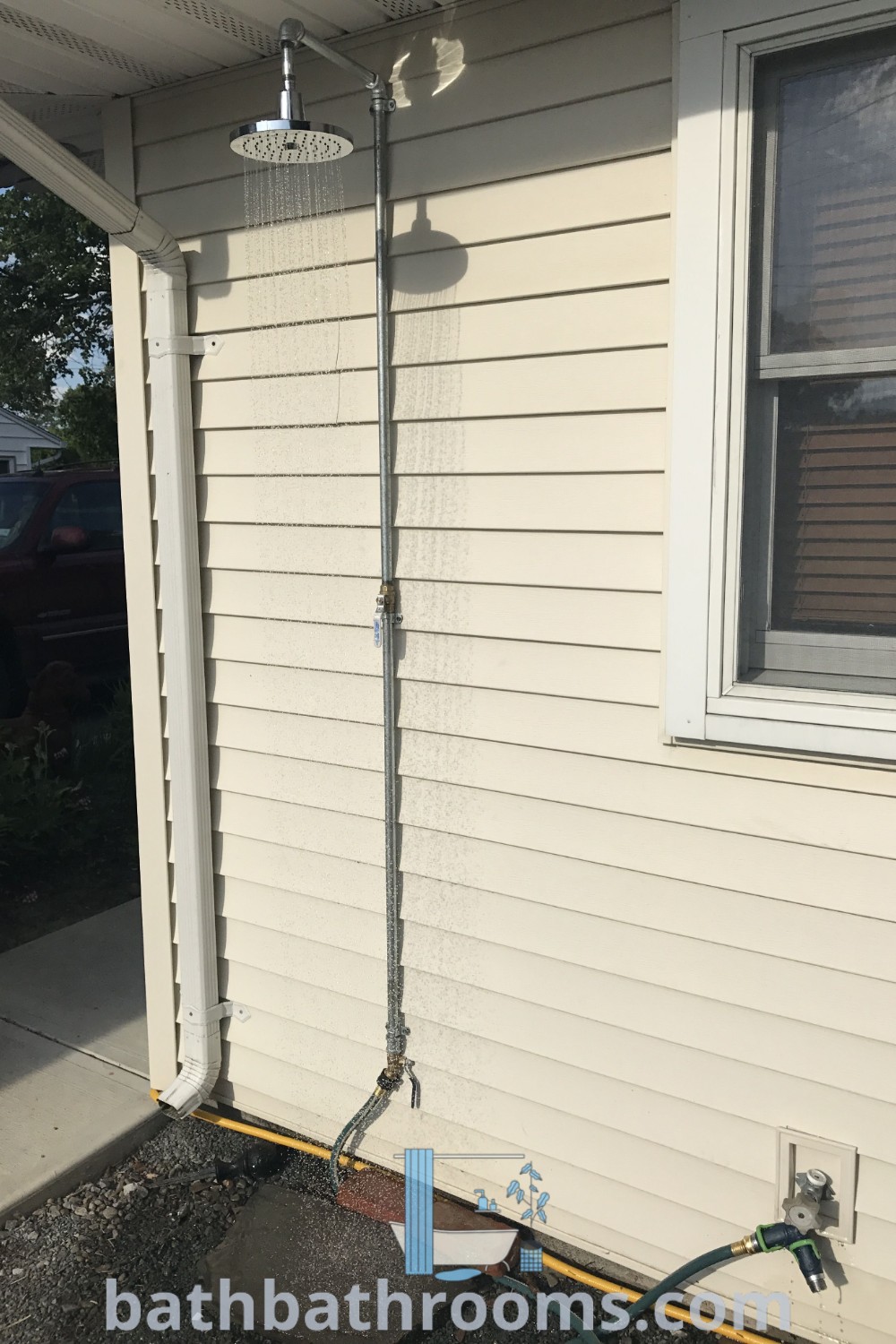 An outdoor shower from a spigot attached to the house, surrounded by hoses, offers a cozy and functional design for your backyard. Explore DIY outdoor shower ideas and inspirations at bathbathrooms.com.