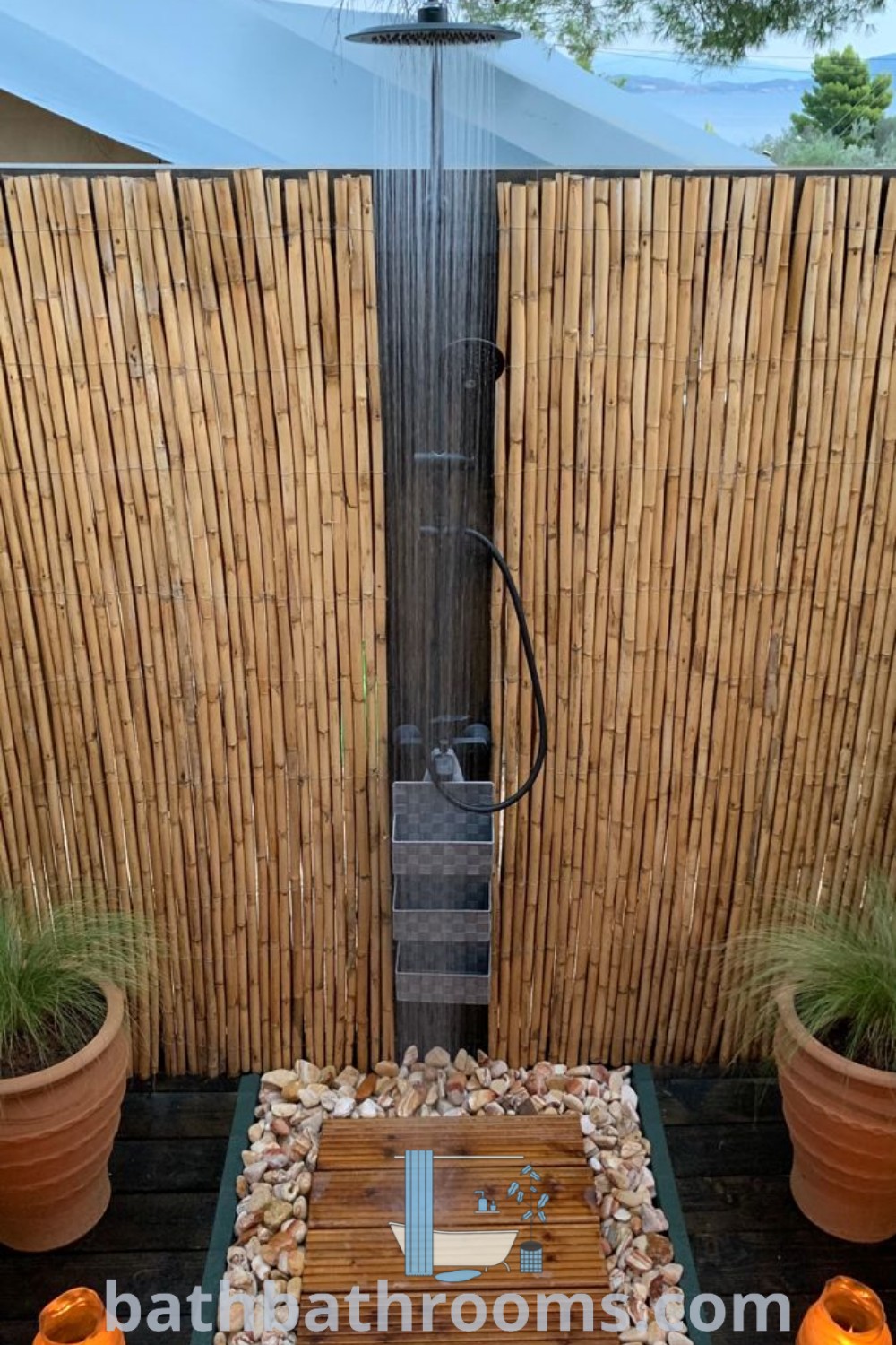 An outdoor shower set in a wooden deck flanked by two potted plants, showcasing inspiring outdoor shower ideas. Explore cozy designs and functional inspirations for your outdoor bathroom design at bathbathrooms.com.