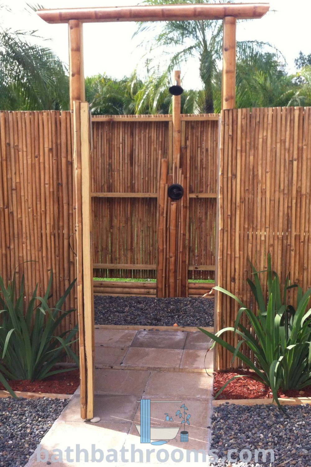 A wooden gate surrounded by vibrant plants and rocks in a garden, complemented by two statues. This inviting outdoor scene showcases unique garden ideas and cozy aesthetics, perfect for enhancing your space. Explore more inspiring decor ideas at bathbathrooms.com.