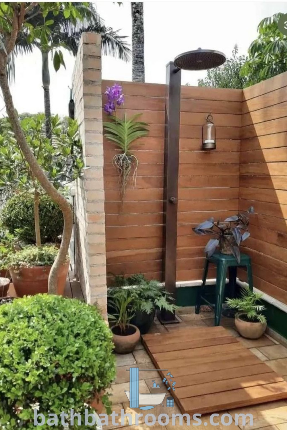 An inviting outdoor shower surrounded by potted plants and trees, showcasing inspiring outdoor bathroom ideas. Perfect for relaxing and enhancing your garden, this design offers a unique fusion of style and nature. Discover more cozy decor ideas at bathbathrooms.com.