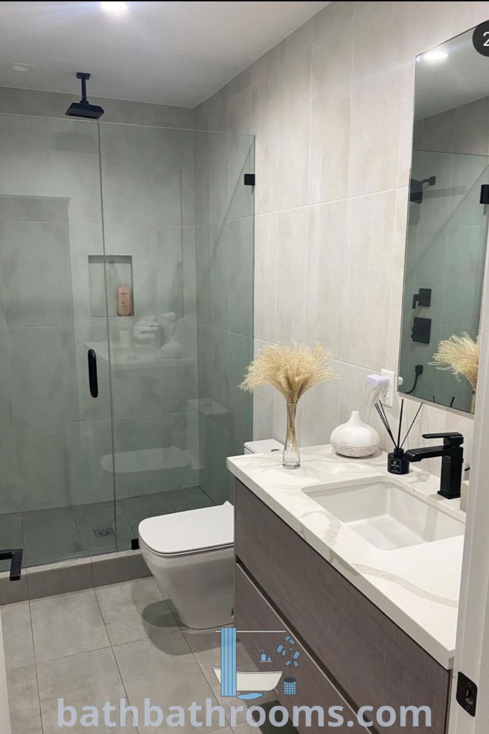 A modern small bathroom featuring a white toilet, sink, mirror, and shower stall that exemplifies minimalist and luxury design. Perfect for cozy homes and New York apartments, this scene provides inspiring decor ideas for those seeking unique aesthetics. Explore more at bathbathrooms.com.