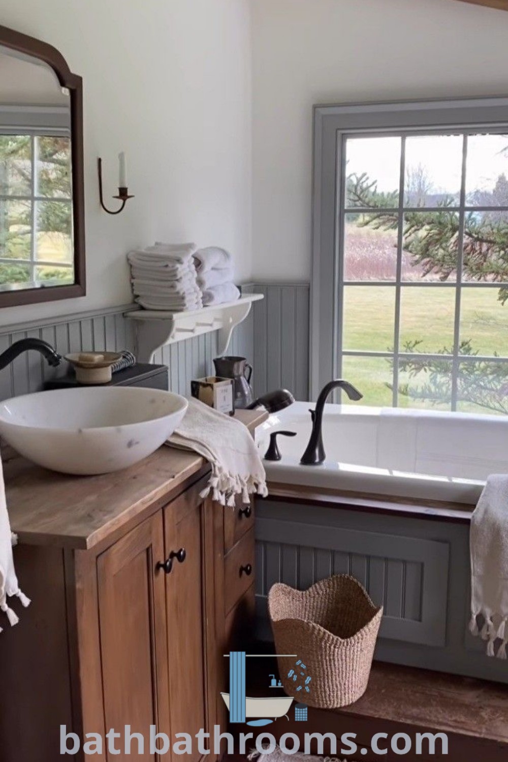 A charming country bathroom with a sink, mirror, and tub next to a window, showcasing Cottage Bedroom Wainscoting and elements from Victorian Cottage and English Country House styles. This cozy design inspires unique ideas for transforming your home. Explore more decor ideas at bathbathrooms.com.