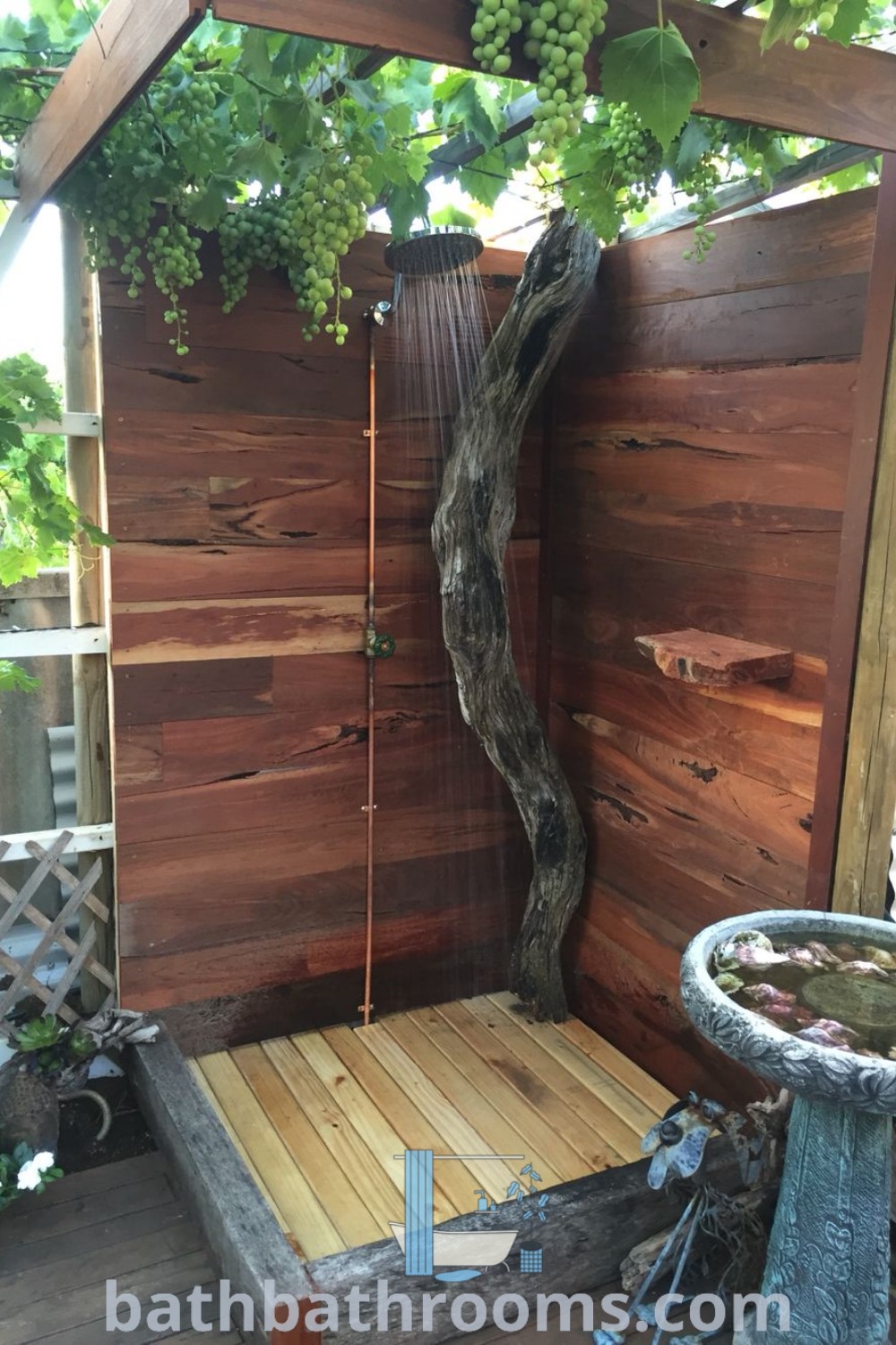 An outdoor shower in a rustic design surrounded by wooden elements and a tree, showcasing cozy outdoors and unique ideas for outdoor shower and compost toilet setups. Explore more decor inspirations at bathbathrooms.com.