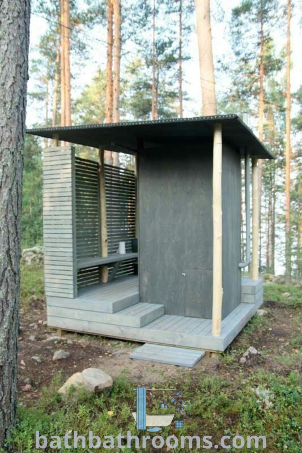 A small outhouse in the woods next to a tree, showcasing modern outdoor toilet design ideas and cozy aesthetics. This cozy restroom exemplifies unique ideas for outdoor toilets and décor inspirations for small spaces. Discover more ideas at bathbathrooms.com.