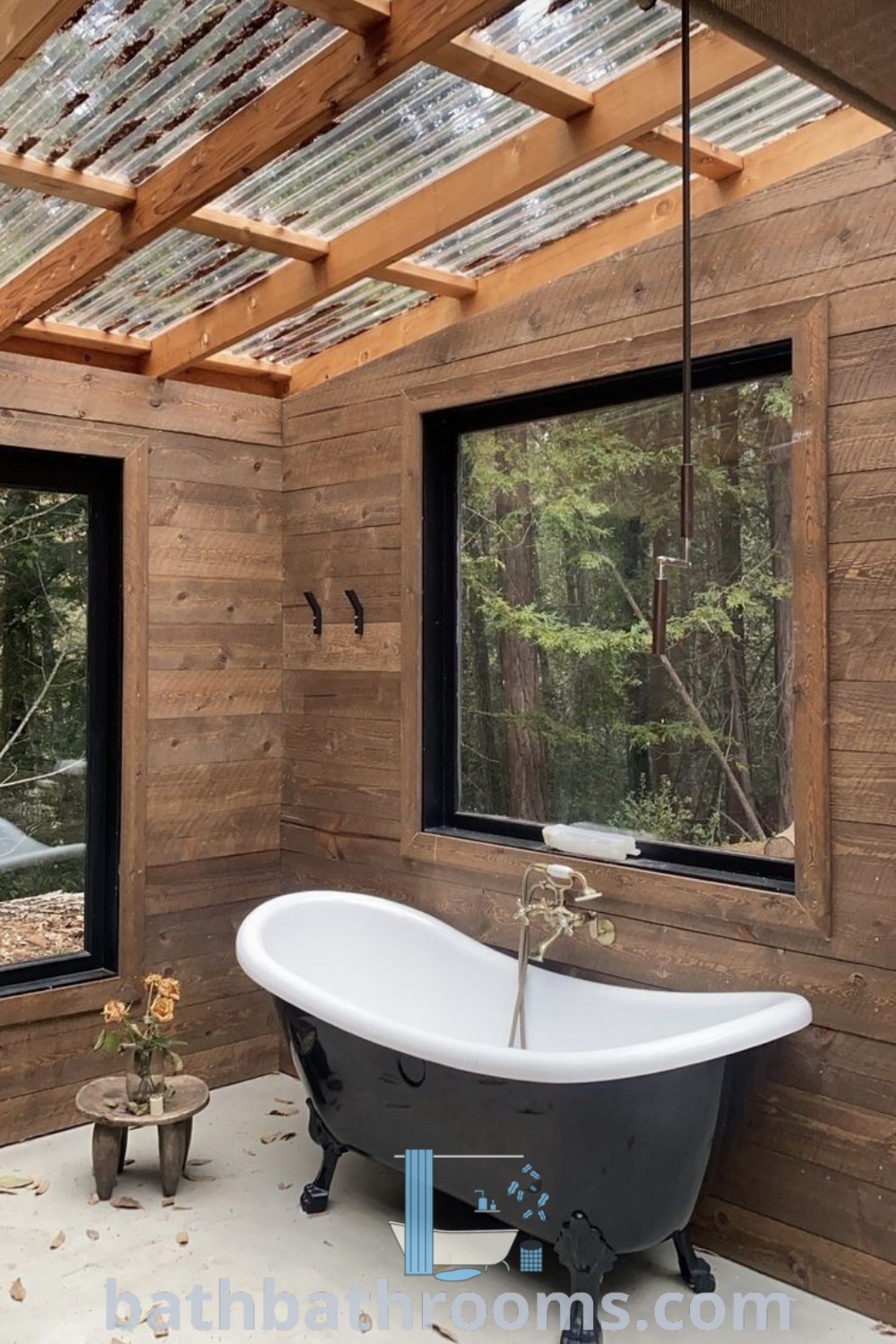A cozy outdoor bathtub set in a room with wooden walls and two windows, surrounded by nature. This design embodies outdoor bathroom ideas perfect for transforming your space into a peaceful retreat. Explore more unique inspirations at bathbathrooms.com.