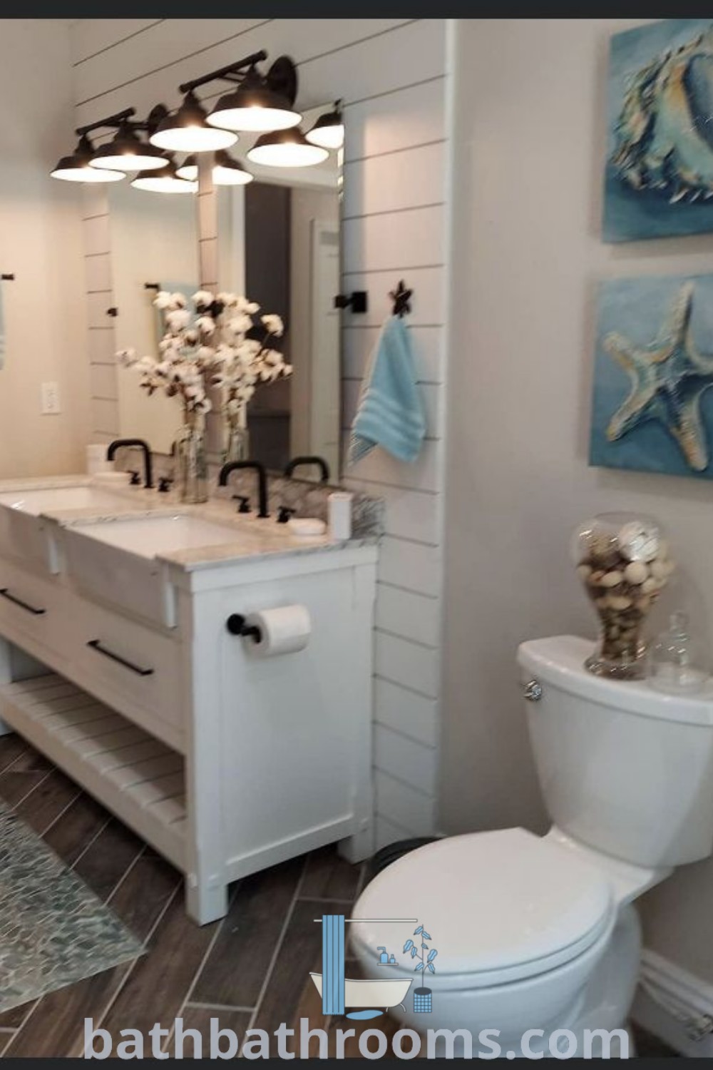 A white toilet adjacent to a sink in a cozy bathroom featuring two pictures on the wall, capturing a Light House Bathroom Theme with coastal decor inspiration. This beach-themed restroom is perfect for guest bathrooms and includes unique designs for a comfortable and stylish aesthetic. Discover more bathroom design ideas at bathbathrooms.com.
