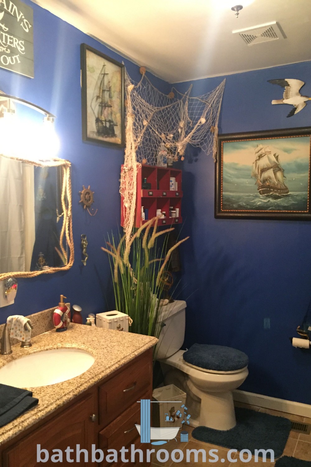A nautical-themed bathroom with blue walls, featuring pictures on the wall and coastal decor elements. Inspired by Tiki and anchor bathroom ideas, it represents cozy aesthetics and functional home decor organization. Explore more inspiring designs at bathbathrooms.com.