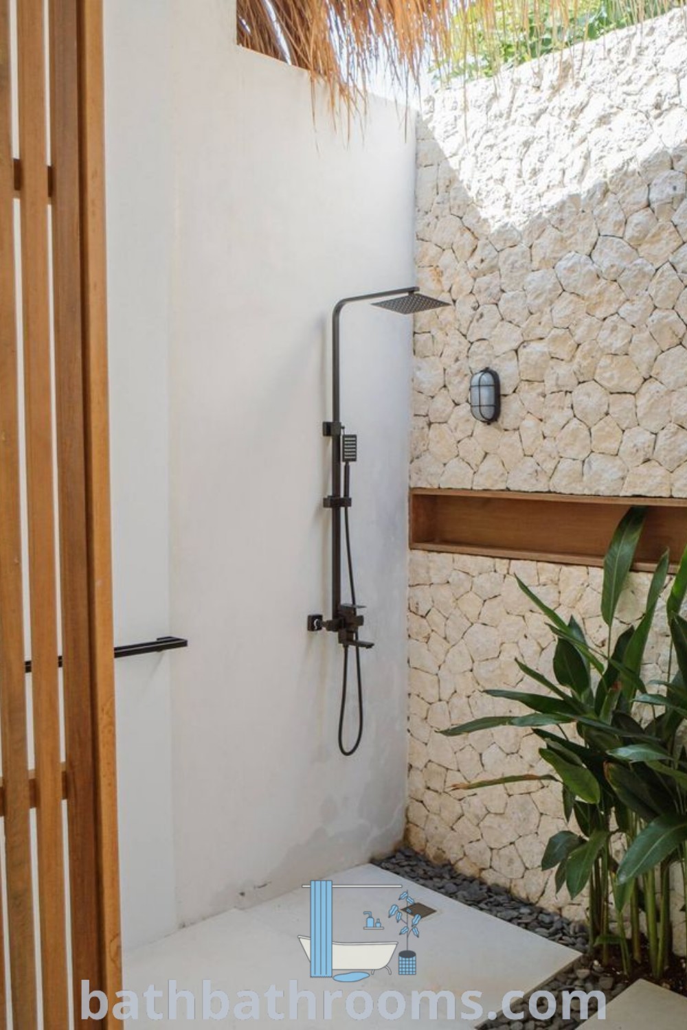 An outdoor bathroom featuring a shower head surrounded by vibrant plants next to a stone wall, showcasing cozy and functional outdoor shower ideas. Discover unique inspirations and design tips for outdoor bathrooms at bathbathrooms.com.