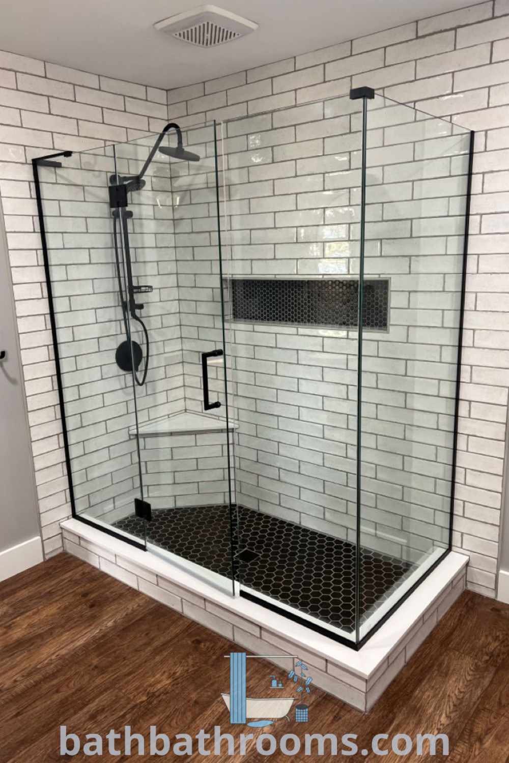 A beautifully designed walk-in shower on a wooden floor, adjacent to a white brick wall, showcasing farmhouse style and cozy decor ideas for a main floor master