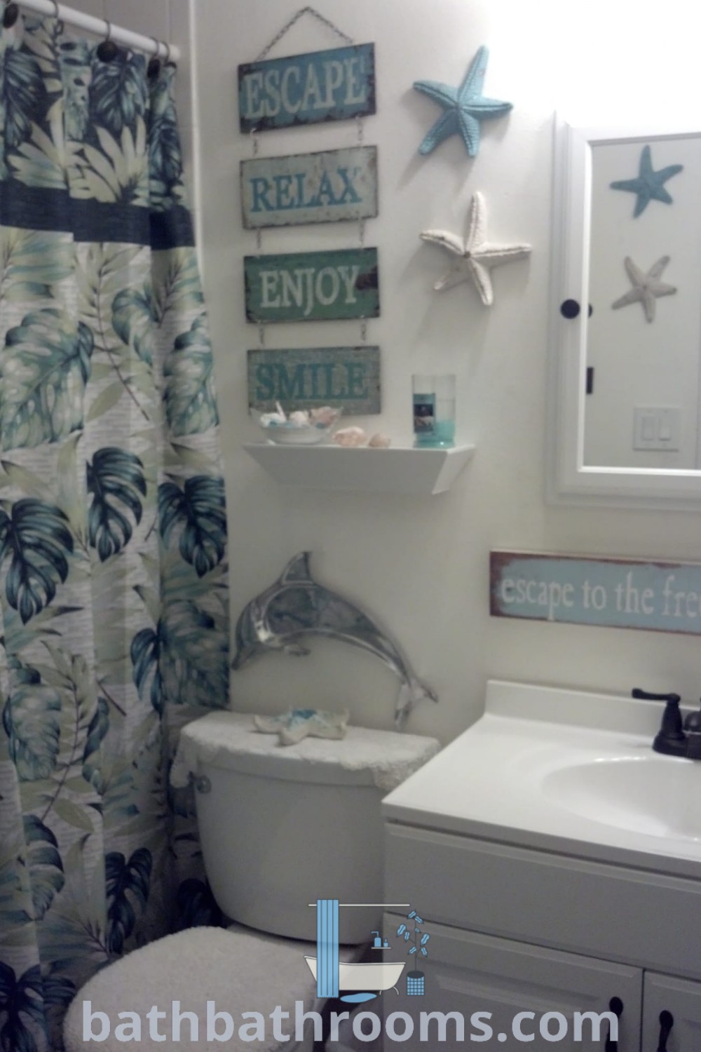 A cozy ocean-themed bathroom featuring a white toilet, bathroom sink, mirror, and shower curtain. This beach bathroom decor embodies a serene coastal vibe, showcasing inspiring ocean-themed design ideas perfect for transforming your space into a relaxing retreat. Discover more at bathbathrooms.com.