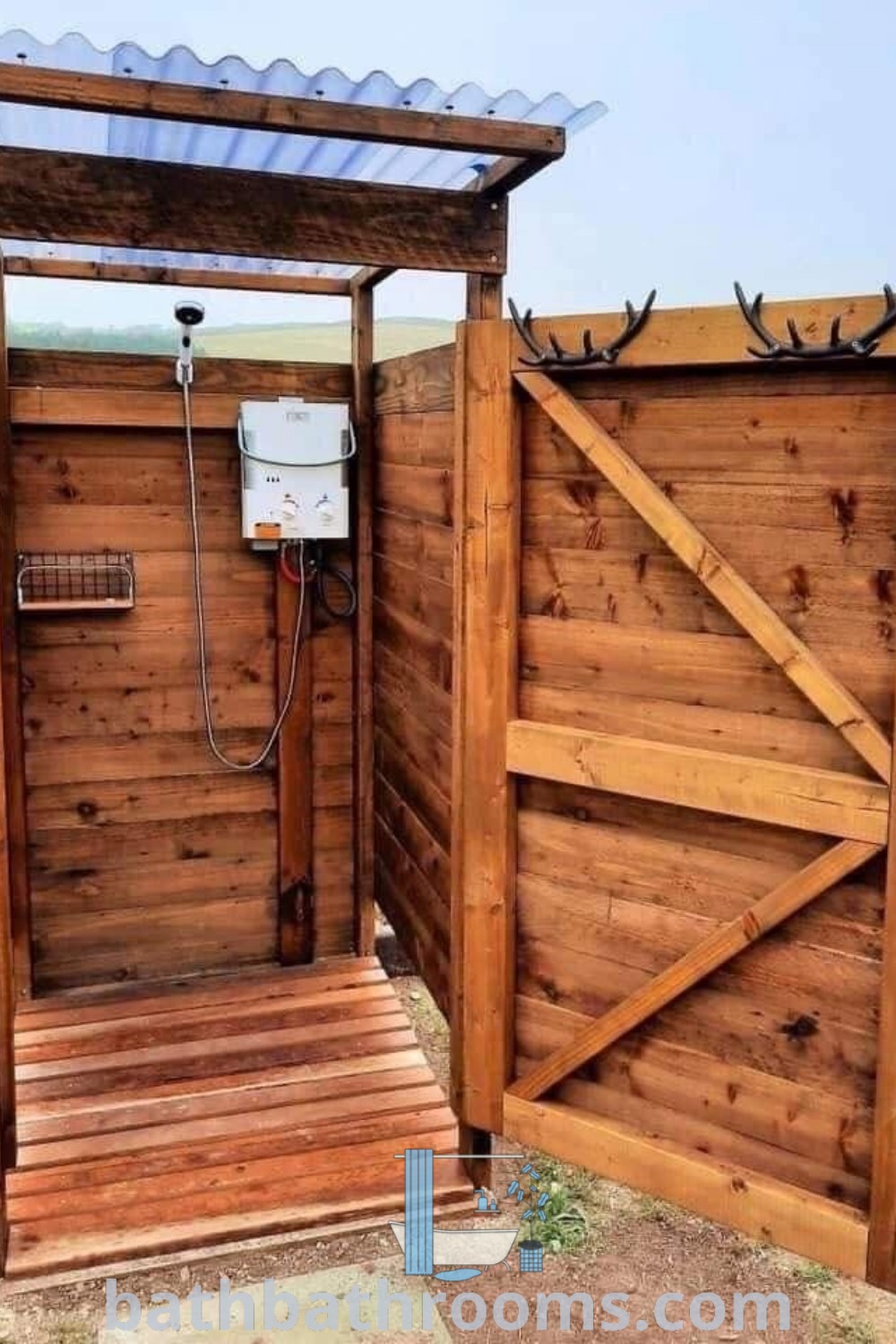 A wooden shower stall with an open door, showcasing a cozy outdoor shower setup that integrates beautifully with nature. This outdoor bathroom design, complete with a stylish toilet inside, offers unique ideas for those looking to enhance their outdoor space. Explore more design ideas at bathbathrooms.com.