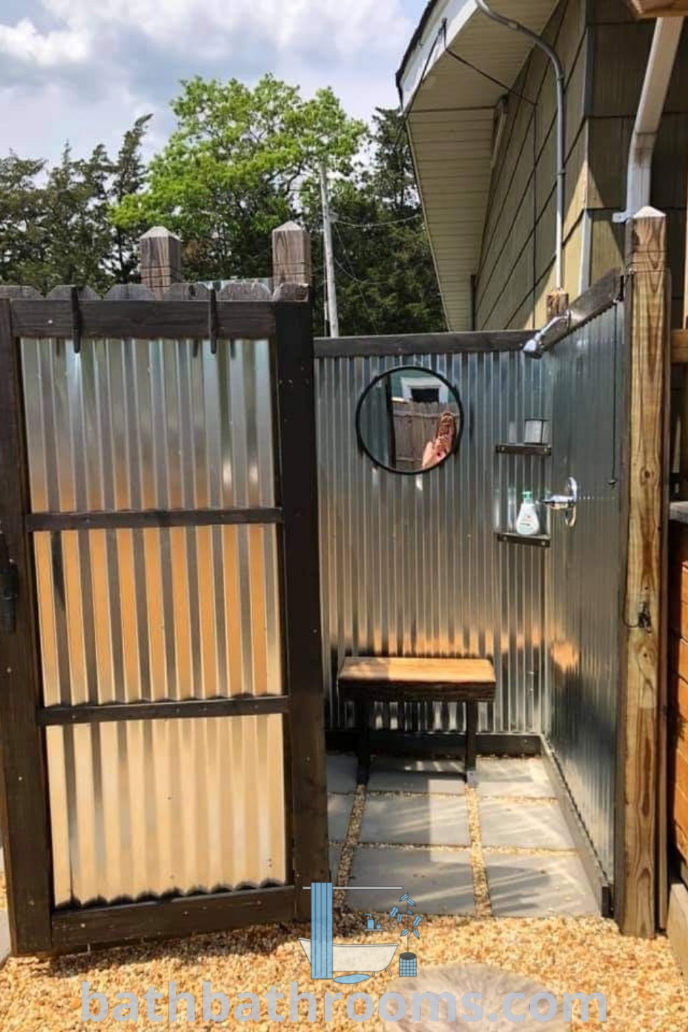 An outdoor shower with a bench and a mirror, designed for an inspiring outdoor restroom, showcasing cozy design ideas. This setup offers functional elegance, perfect for enhancing backyard spaces. Discover more outdoor shower inspirations at bathbathrooms.com.