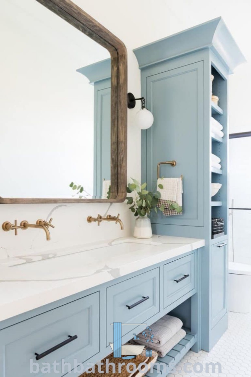 A cozy small bathroom featuring blue cabinetry, white countertops, and a large mirror above the sink. This beach house interior design combines style with functionality, offering inspiring decor ideas for maximizing space. Visit bathbathrooms.com for more design inspirations.