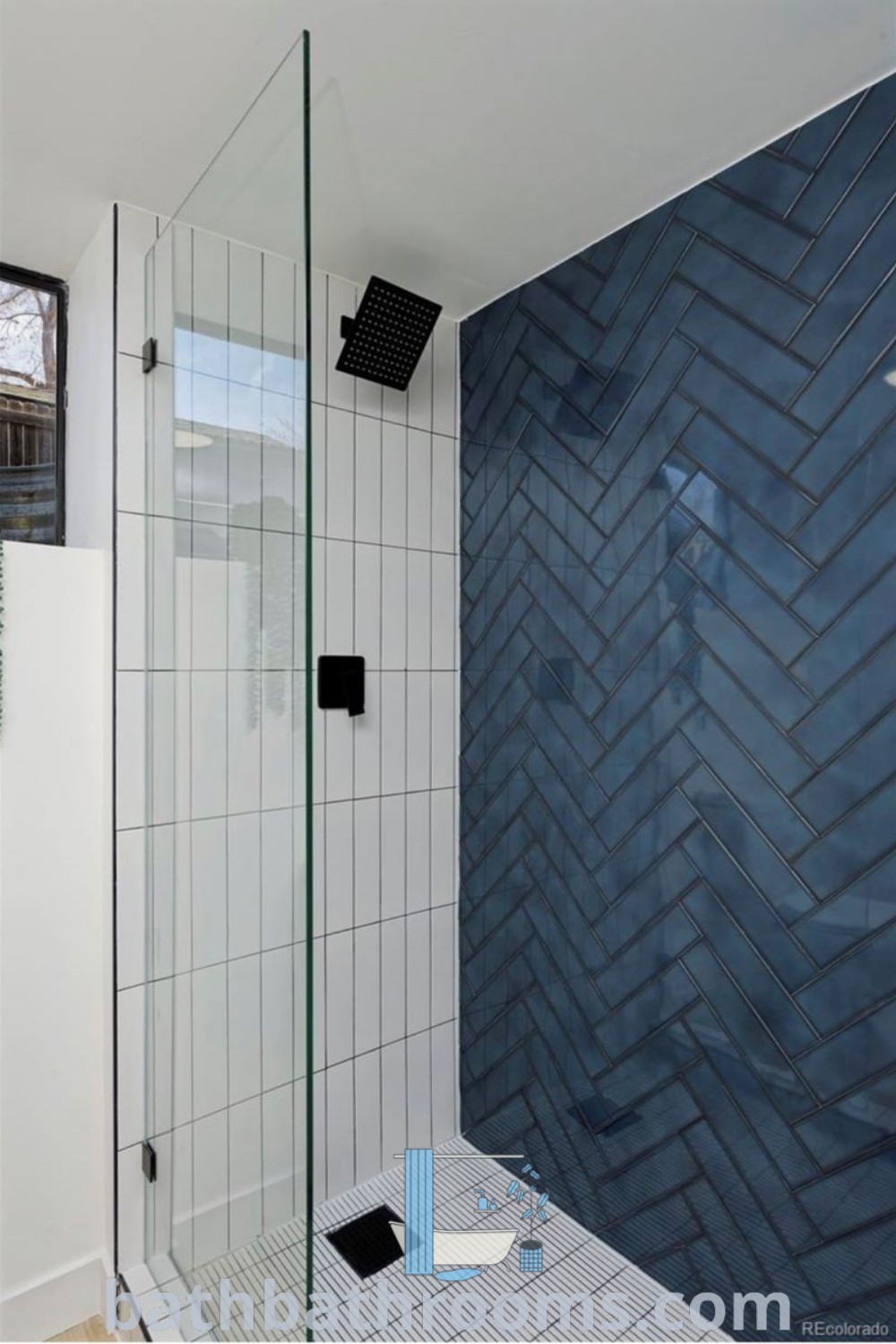 A bathroom featuring a walk-in shower next to a blue tiled wall and a white tile floor, showcasing masculine blue shower designs with dark blue herringbone tile. Discover more decor ideas at bathbathrooms.com.